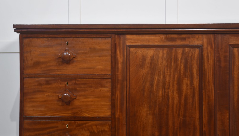 A 19th-century low mahogany linen press with a central double-door cupboard flanked by ten drawers with turned wooden knobs. View II