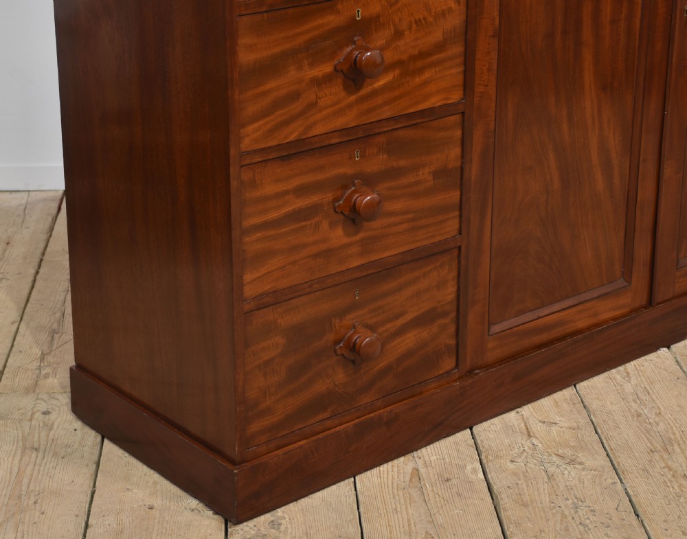 A 19th-century low mahogany linen press with a central double-door cupboard flanked by ten drawers with turned wooden knobs. View X