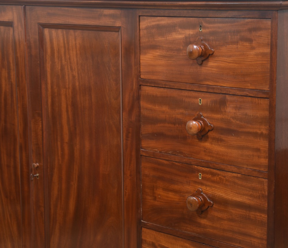 A 19th-century low mahogany linen press with a central double-door cupboard flanked by ten drawers with turned wooden knobs. View XII