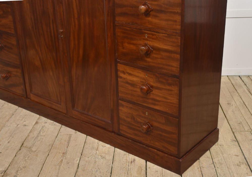 A 19th-century low mahogany linen press with a central double-door cupboard flanked by ten drawers with turned wooden knobs. View XIII