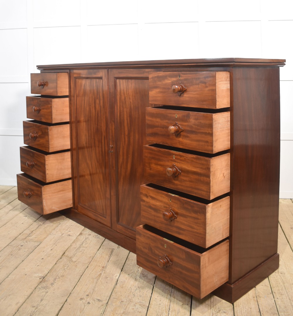 A 19th-century low mahogany linen press with a central double-door cupboard flanked by ten drawers with turned wooden knobs. View XIV