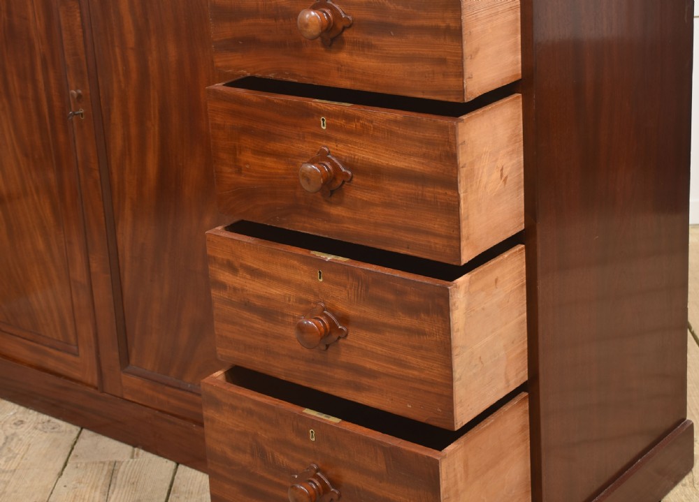 A 19th-century low mahogany linen press with a central double-door cupboard flanked by ten drawers with turned wooden knobs. View XV
