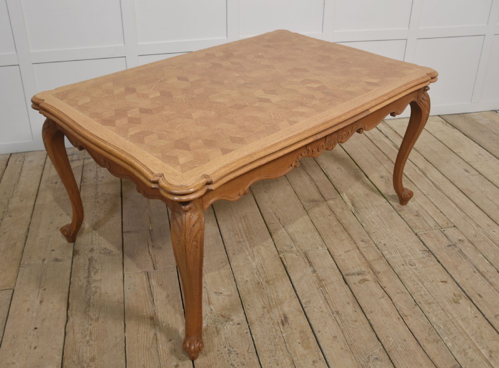 An oak dining table featuring a geometric parquetry top, scalloped corners, carved apron detailing, and cabriole legs.