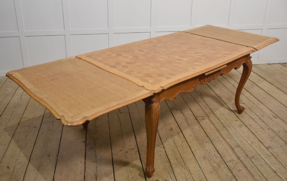 An oak dining table featuring a geometric parquetry top, scalloped corners, carved apron detailing, and cabriole legs. View II