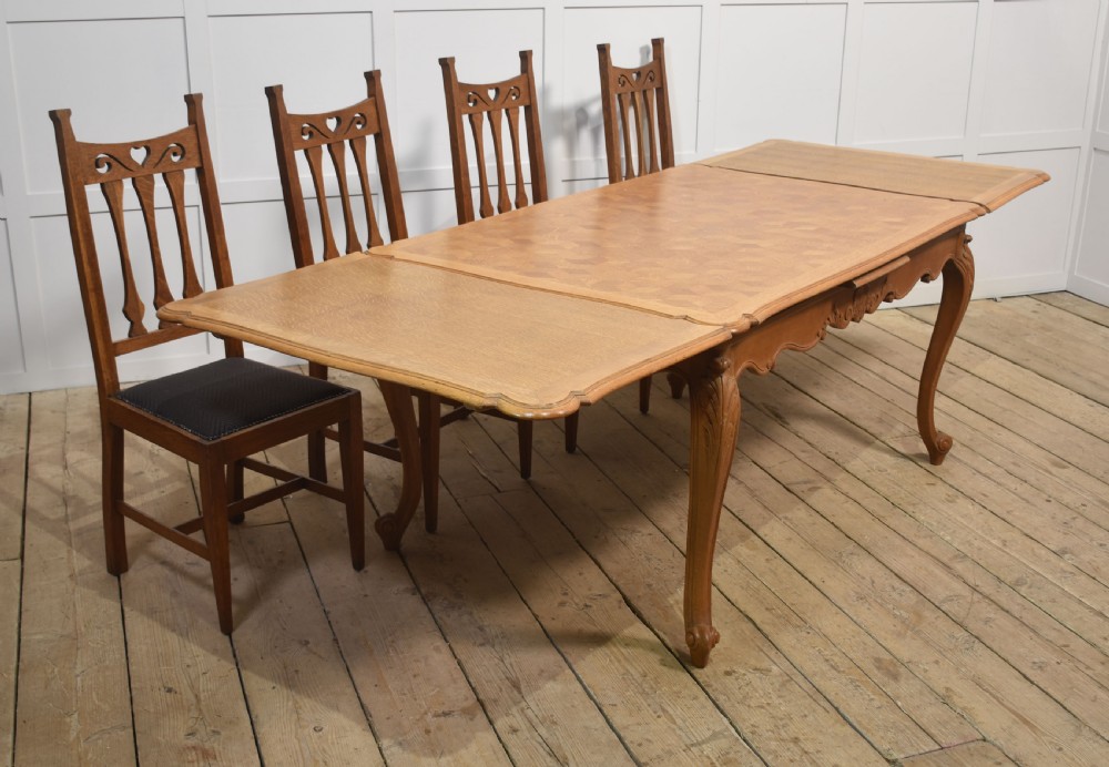 An oak dining table featuring a geometric parquetry top, scalloped corners, carved apron detailing, and cabriole legs. View III
