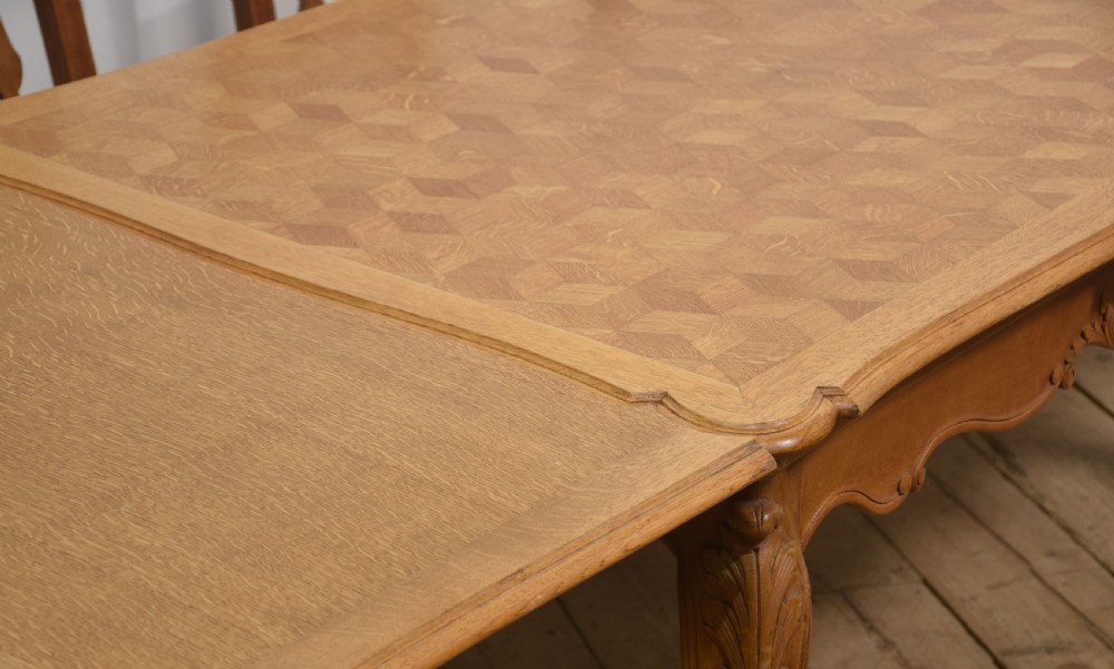 An oak dining table featuring a geometric parquetry top, scalloped corners, carved apron detailing, and cabriole legs. View V
