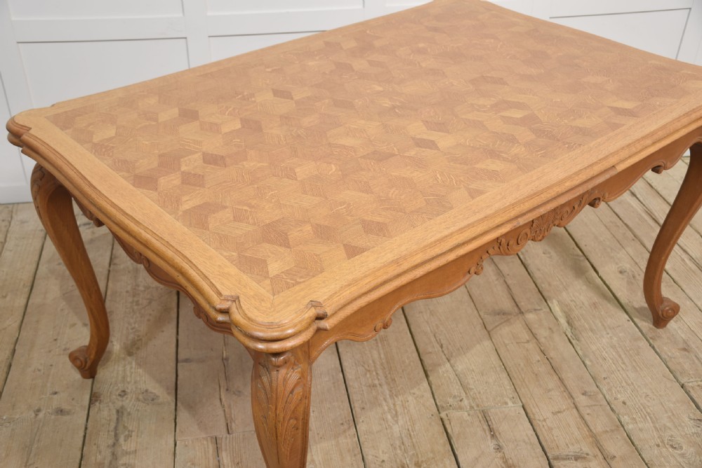 An oak dining table featuring a geometric parquetry top, scalloped corners, carved apron detailing, and cabriole legs. View IX
