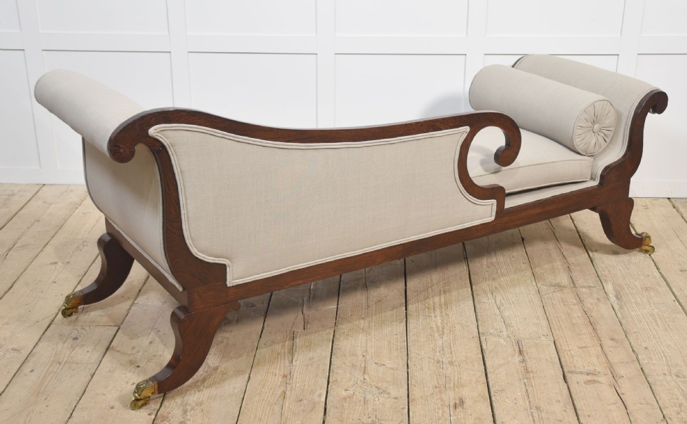 A Regency rosewood chaise longue with carved scroll arms, light grey fabric upholstery, matching bolster cushions, and brass castors. View XII