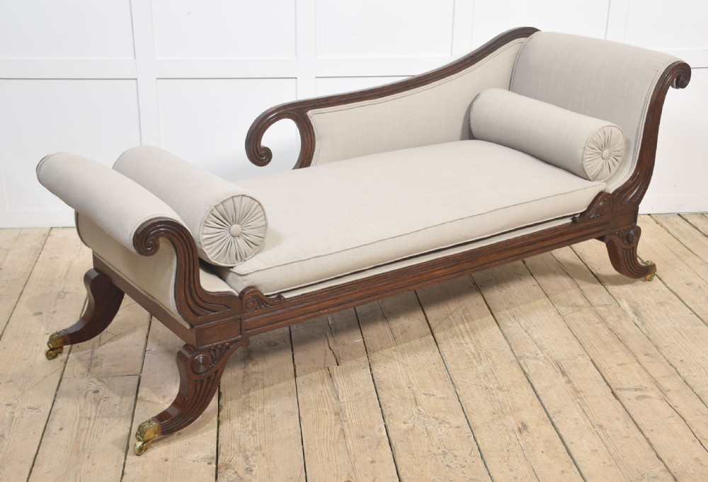 A Regency rosewood chaise longue with carved scroll arms, light grey fabric upholstery, matching bolster cushions, and brass castors. View XIII