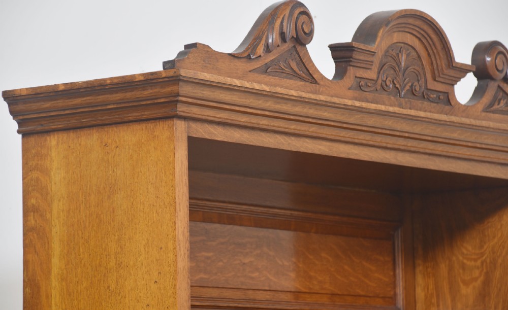 A warm brown oak dresser featuring a carved scrollwork pediment, leaded glass upper cabinet doors, a central mirror insert, a single long drawer, and double lower doors with geometric panel carving. View X
