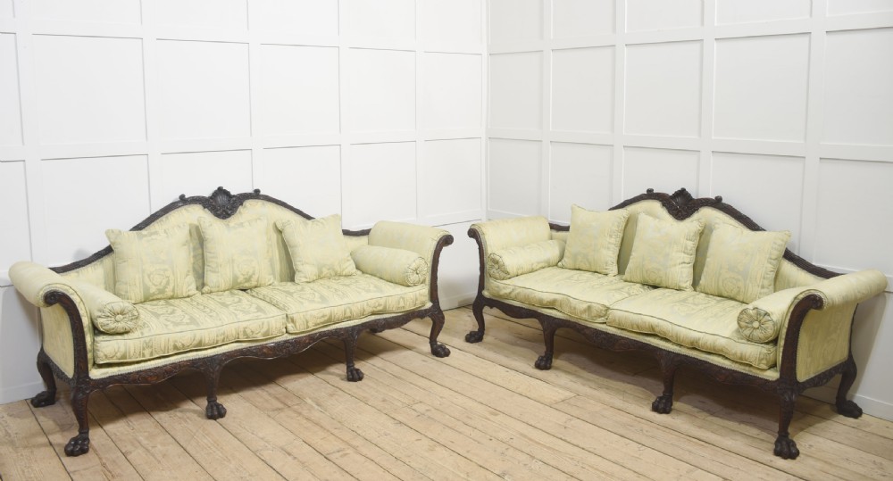 A pair of carved dark mahogany Chippendale revival settees upholstered in light sage patterned fabric with ball-and-claw feet.
