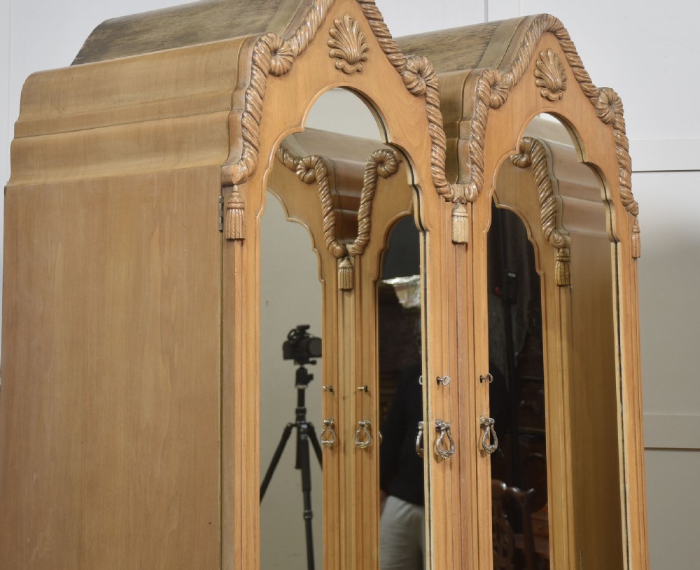 A near pair of tall light walnut wardrobes featuring twin arched mirrored doors, rope-twist carved borders, shell motifs, and two base drawers on carved feet. View II