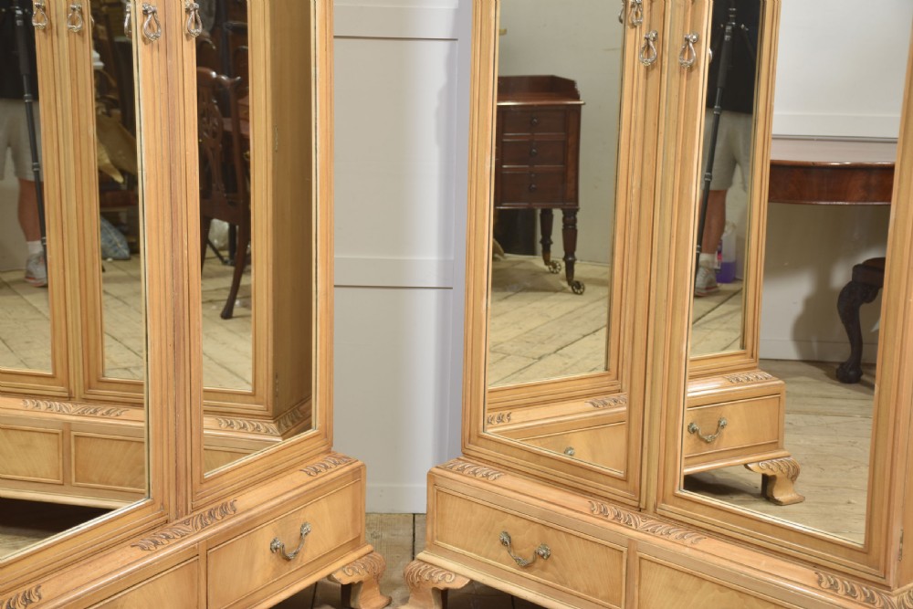 A near pair of tall light walnut wardrobes featuring twin arched mirrored doors, rope-twist carved borders, shell motifs, and two base drawers on carved feet. View VI