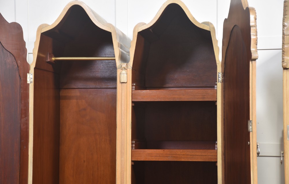 A near pair of tall light walnut wardrobes featuring twin arched mirrored doors, rope-twist carved borders, shell motifs, and two base drawers on carved feet. View X
