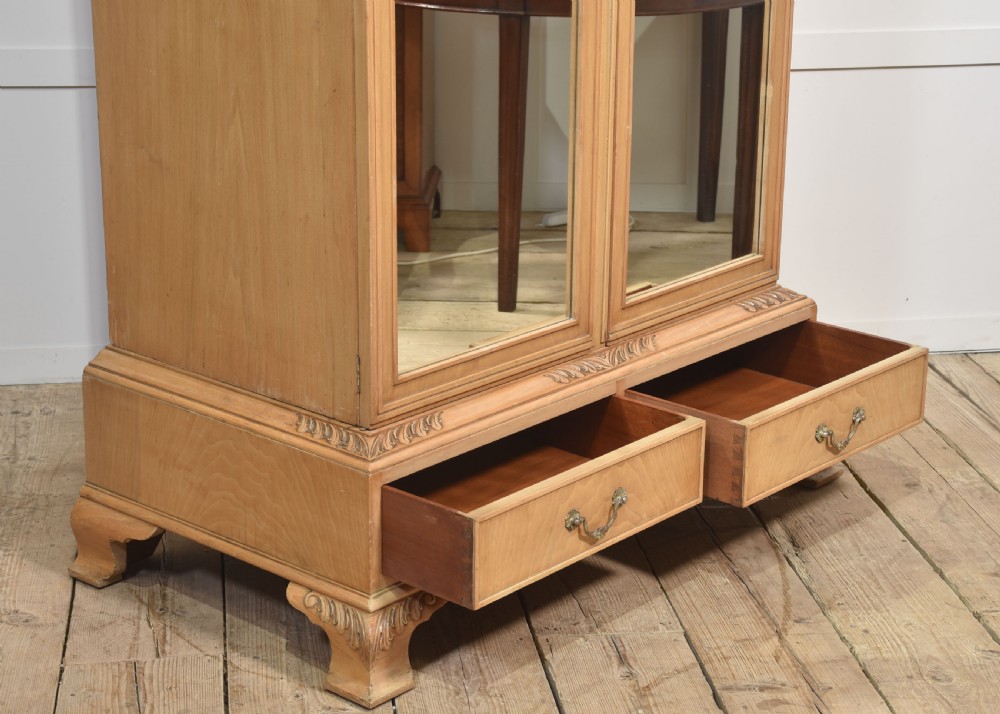 A near pair of tall light walnut wardrobes featuring twin arched mirrored doors, rope-twist carved borders, shell motifs, and two base drawers on carved feet. View XVI