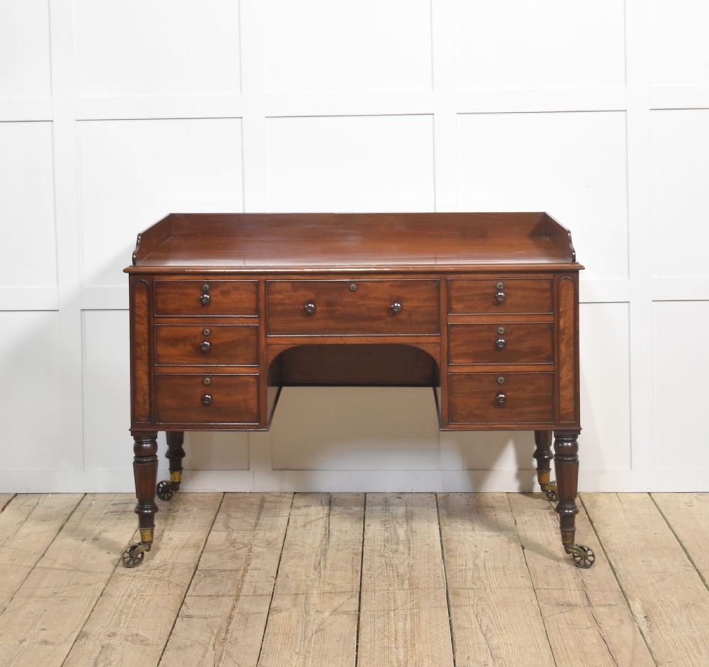 A 19th-century mahogany writing desk featuring seven drawers with dark wooden knobs, a low gallery back, turned legs, and brass castors.