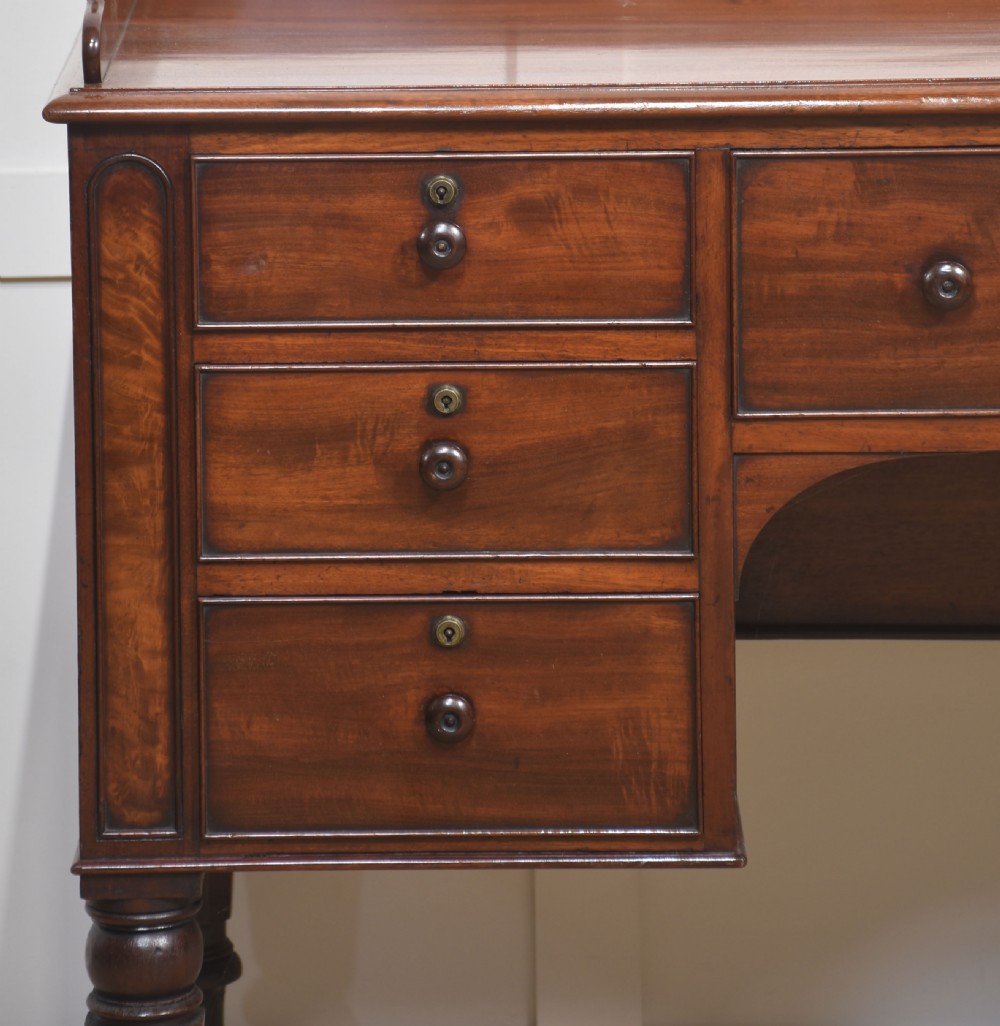 A 19th-century mahogany writing desk featuring seven drawers with dark wooden knobs, a low gallery back, turned legs, and brass castors. View VIII