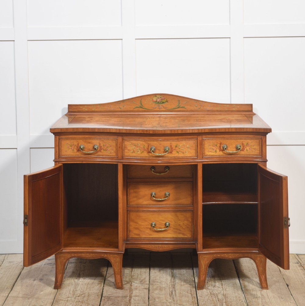 An antique painted satinwood dressing table featuring floral artwork, a central kneehole, side cupboards, drawers, brass handles, and a low gallery back. View III