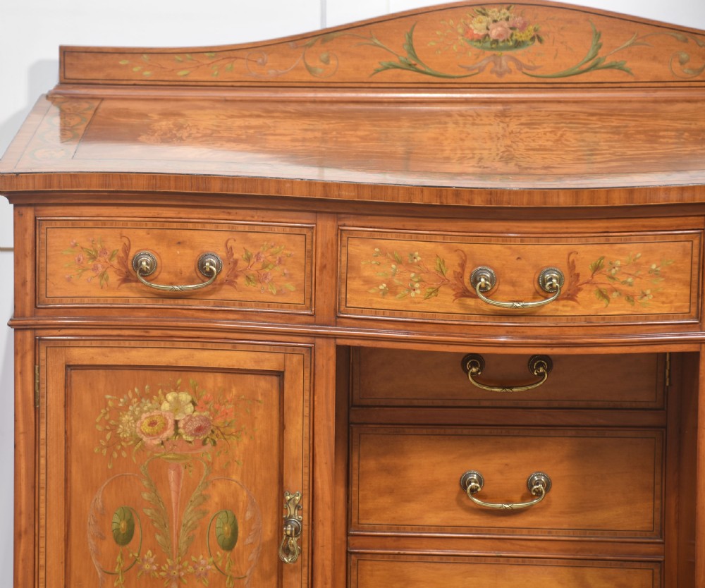 An antique painted satinwood dressing table featuring floral artwork, a central kneehole, side cupboards, drawers, brass handles, and a low gallery back. View VI