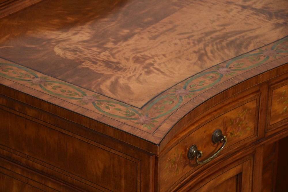 An antique painted satinwood dressing table featuring floral artwork, a central kneehole, side cupboards, drawers, brass handles, and a low gallery back. View XI