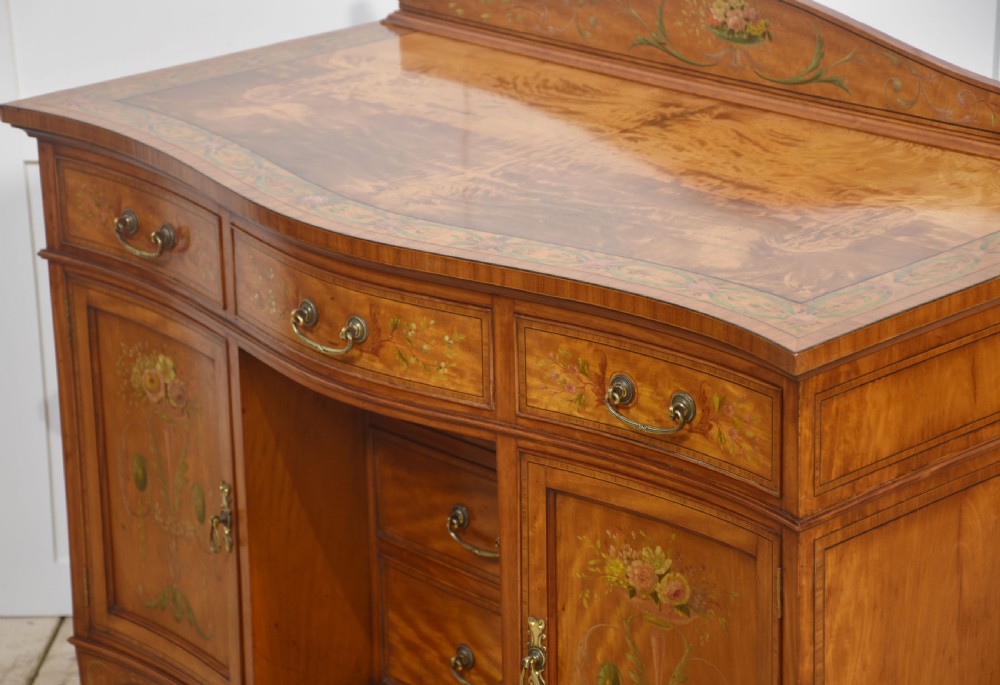 An antique painted satinwood dressing table featuring floral artwork, a central kneehole, side cupboards, drawers, brass handles, and a low gallery back. View XIV