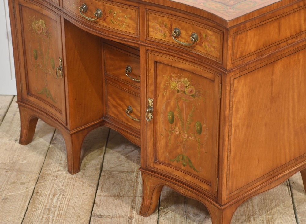 An antique painted satinwood dressing table featuring floral artwork, a central kneehole, side cupboards, drawers, brass handles, and a low gallery back. View XV