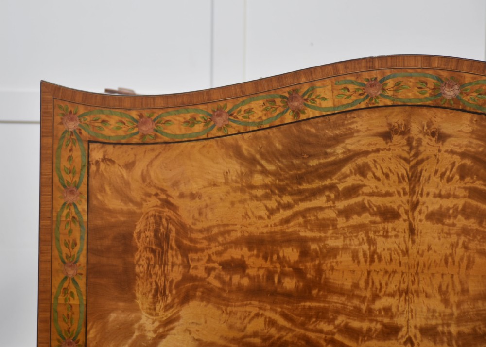 An antique painted satinwood dressing table featuring floral artwork, a central kneehole, side cupboards, drawers, brass handles, and a low gallery back. View XVII