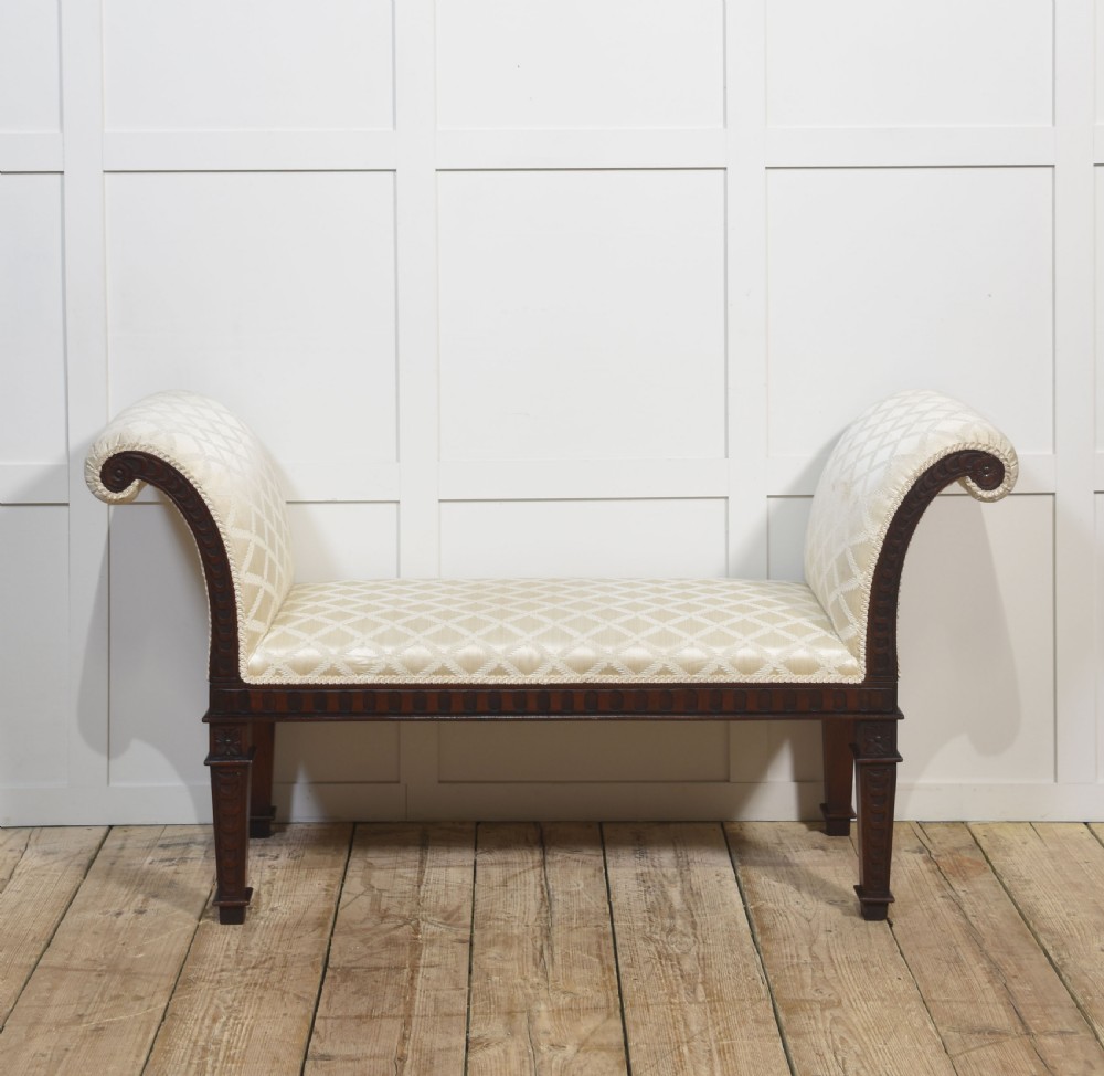 A carved mahogany window seat with out-curved scrolled arms, cream diamond-patterned fabric upholstery, and square tapered legs.