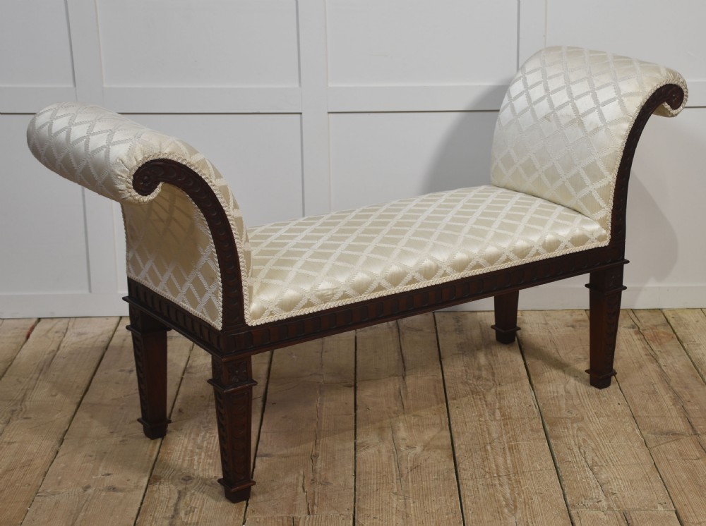 A carved mahogany window seat with out-curved scrolled arms, cream diamond-patterned fabric upholstery, and square tapered legs. View VII