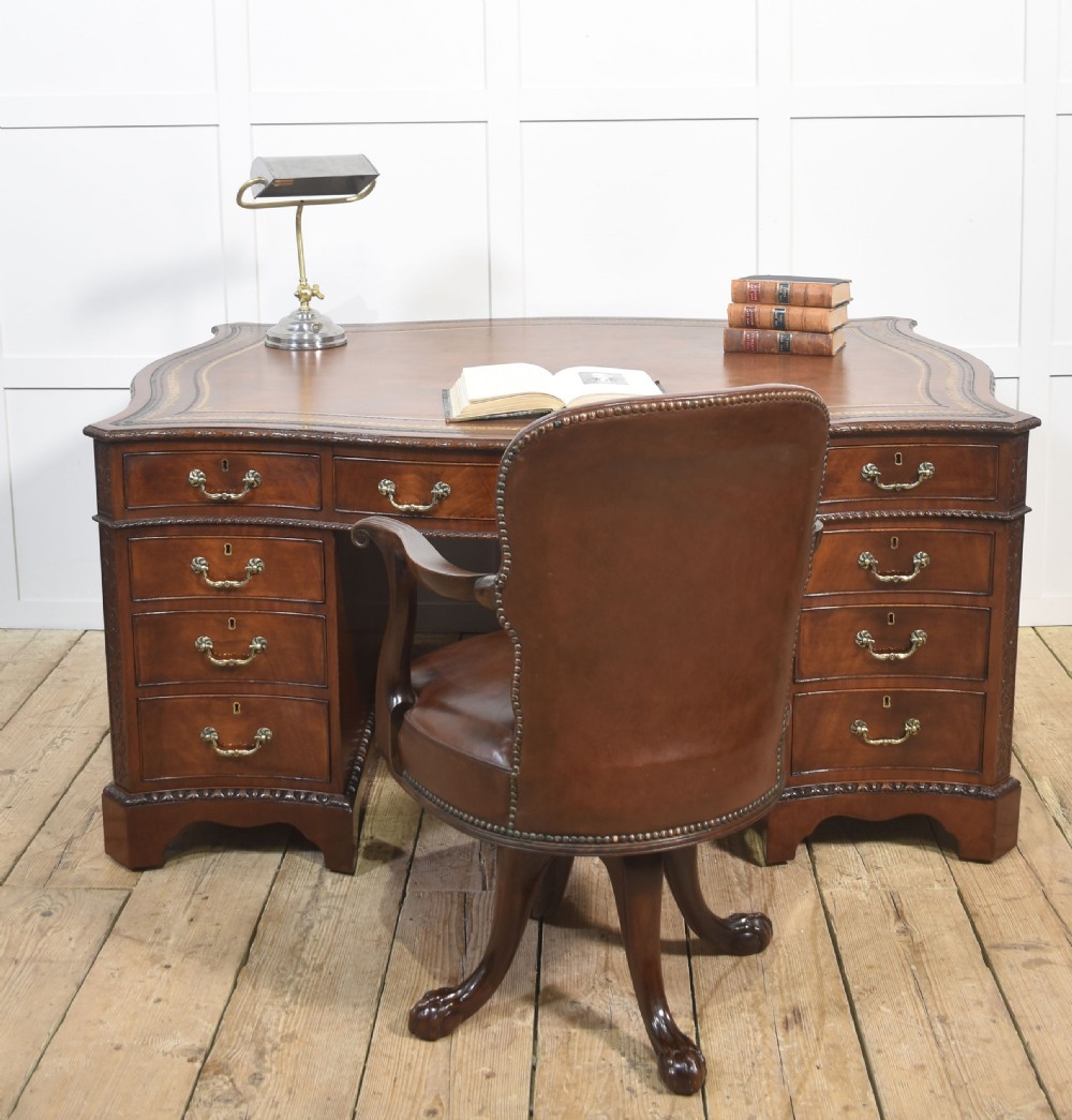 A large Chippendale Revival mahogany partners desk with a serpentine front, gilded leather inset writing top, and brass swan-neck handles. View II