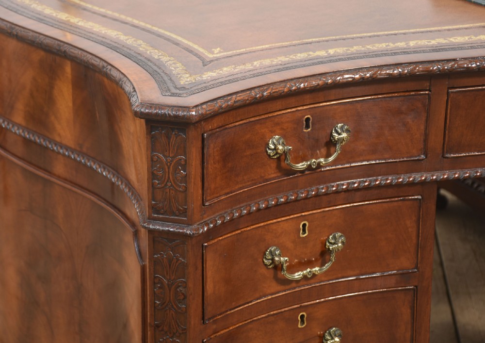 A large Chippendale Revival mahogany partners desk with a serpentine front, gilded leather inset writing top, and brass swan-neck handles. View VII
