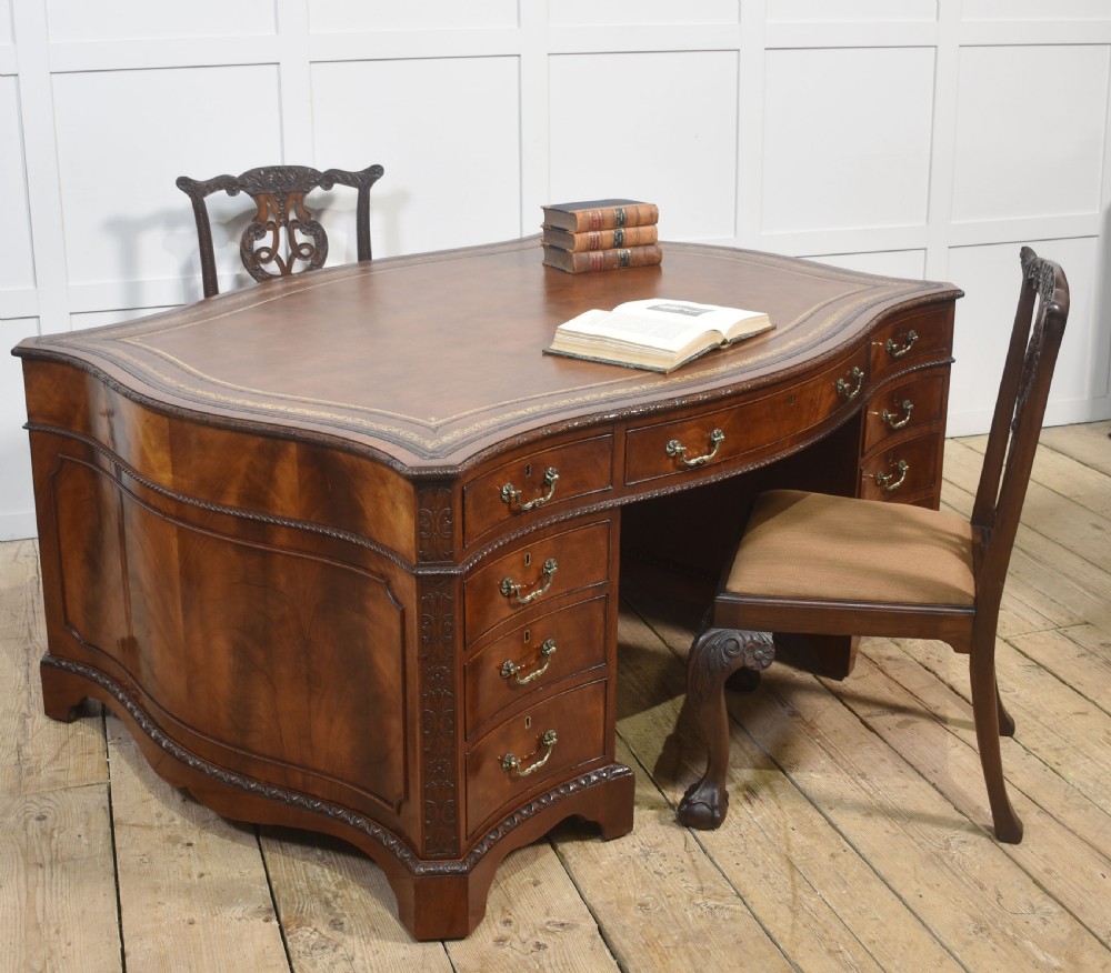 A large Chippendale Revival mahogany partners desk with a serpentine front, gilded leather inset writing top, and brass swan-neck handles. View VIII