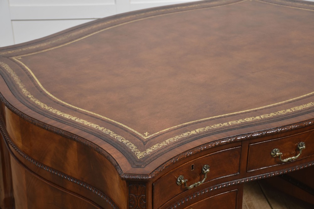 A large Chippendale Revival mahogany partners desk with a serpentine front, gilded leather inset writing top, and brass swan-neck handles. View XI