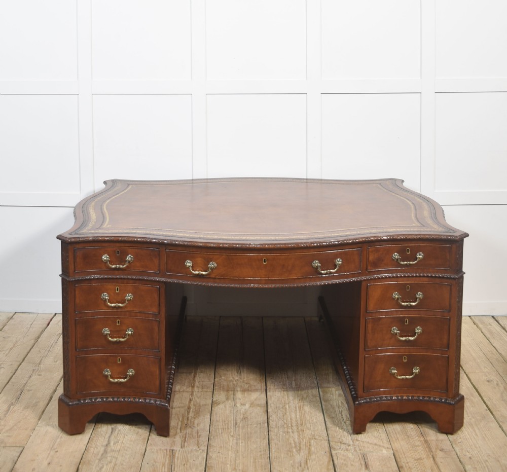 A large Chippendale Revival mahogany partners desk with a serpentine front, gilded leather inset writing top, and brass swan-neck handles. View XII