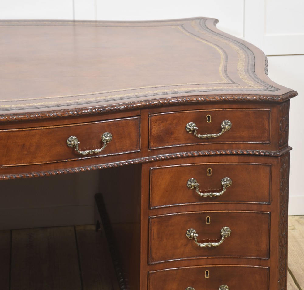 A large Chippendale Revival mahogany partners desk with a serpentine front, gilded leather inset writing top, and brass swan-neck handles. View XIII
