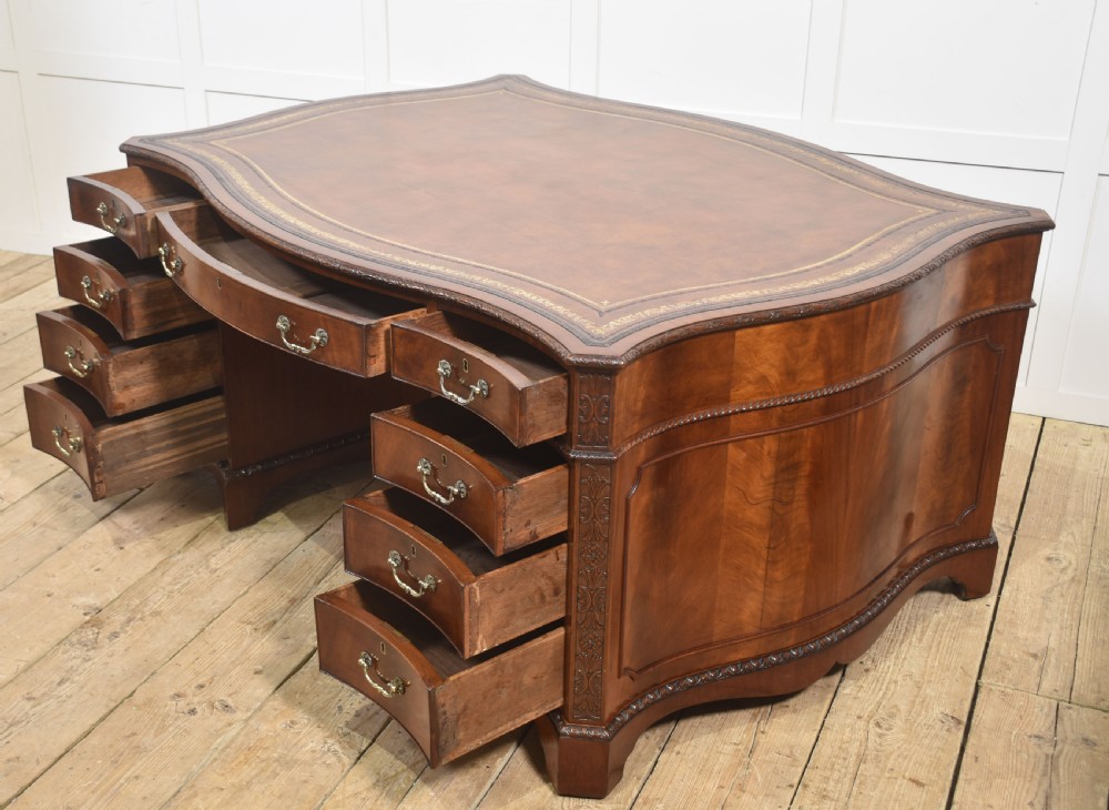 A large Chippendale Revival mahogany partners desk with a serpentine front, gilded leather inset writing top, and brass swan-neck handles. View XV