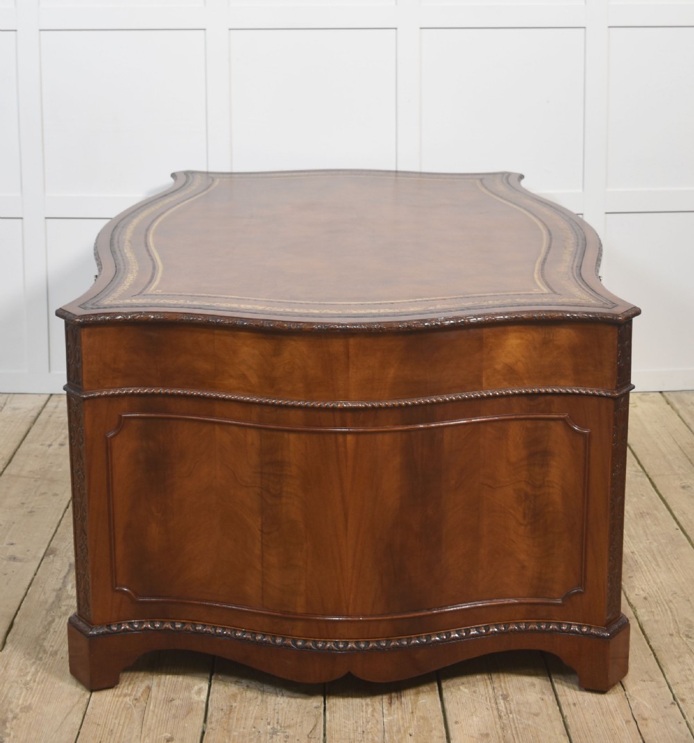 A large Chippendale Revival mahogany partners desk with a serpentine front, gilded leather inset writing top, and brass swan-neck handles. View XVI
