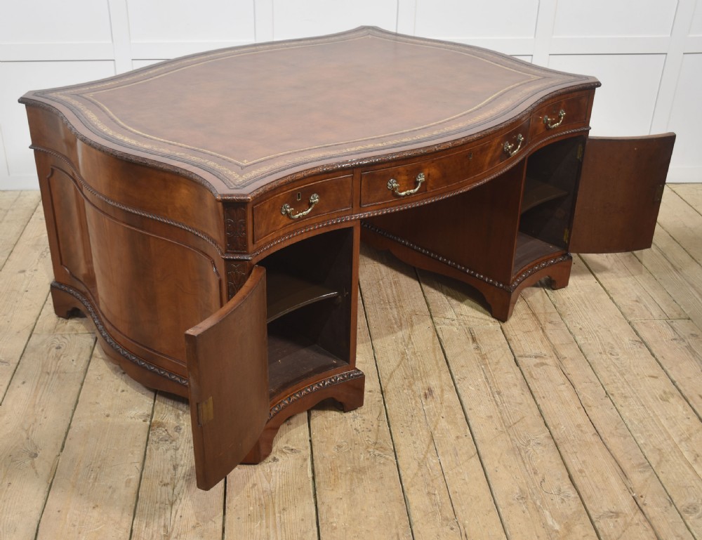 A large Chippendale Revival mahogany partners desk with a serpentine front, gilded leather inset writing top, and brass swan-neck handles. View XVIII
