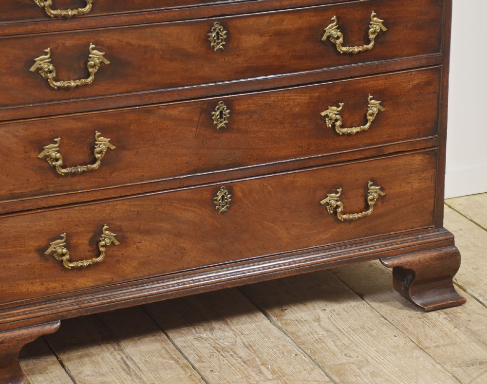A George III mahogany bureau featuring a sloping fall-front lid above four graduated drawers with brass handles and bracket feet. View V