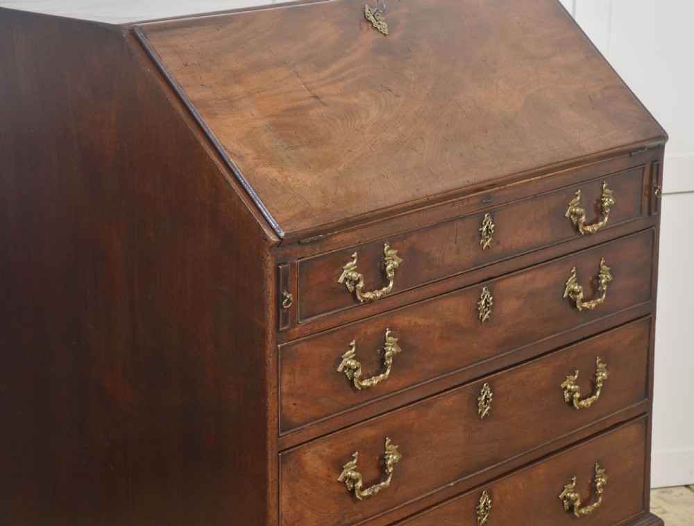 A George III mahogany bureau featuring a sloping fall-front lid above four graduated drawers with brass handles and bracket feet. View X