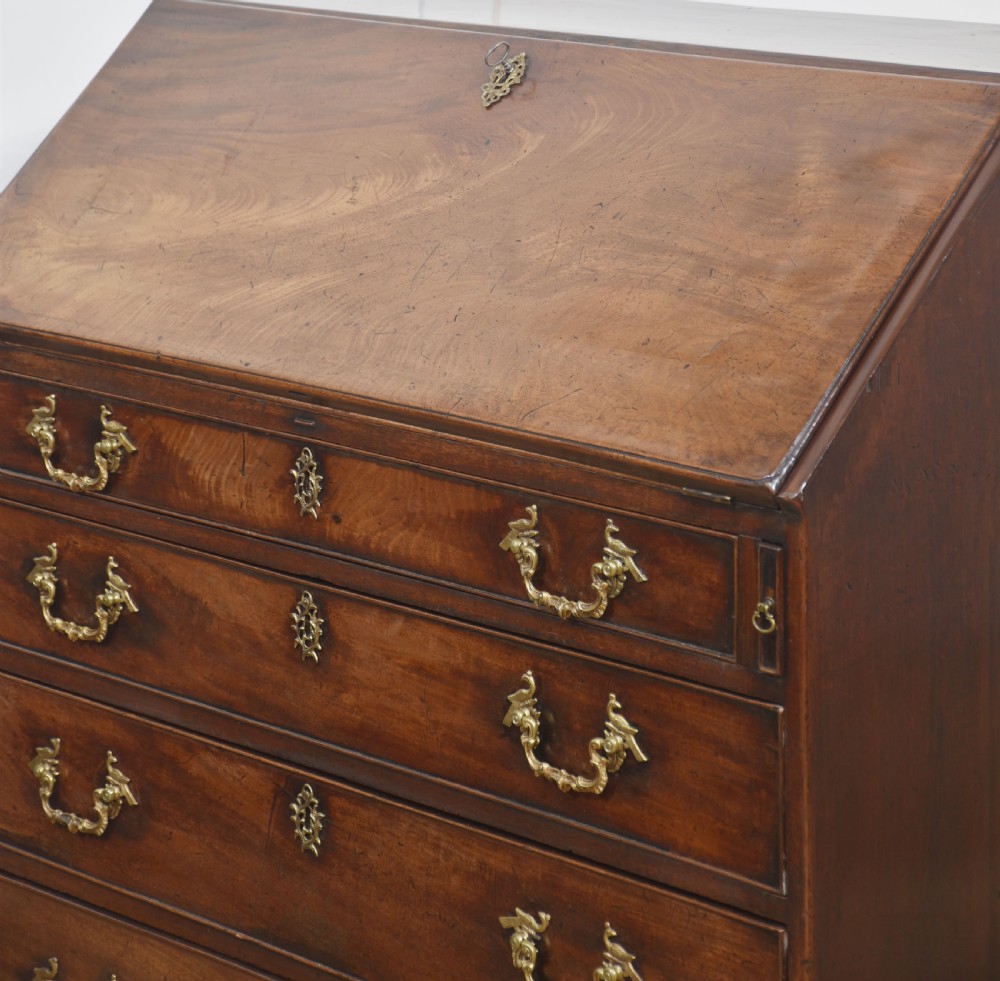 A George III mahogany bureau featuring a sloping fall-front lid above four graduated drawers with brass handles and bracket feet. View XIV
