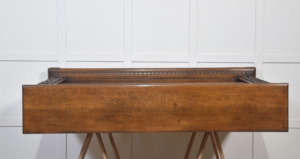 A low carved dark oak open bookcase featuring three wide shelves flanked by carved foliate borders and a central shield motif. View XIV