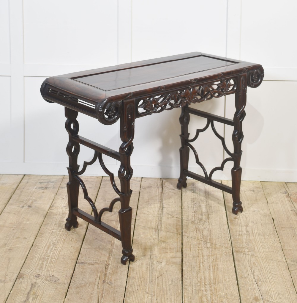 A dark hardwood Chinese altar table featuring openwork carved aprons, everted flanges, and decorative carved stretchers.