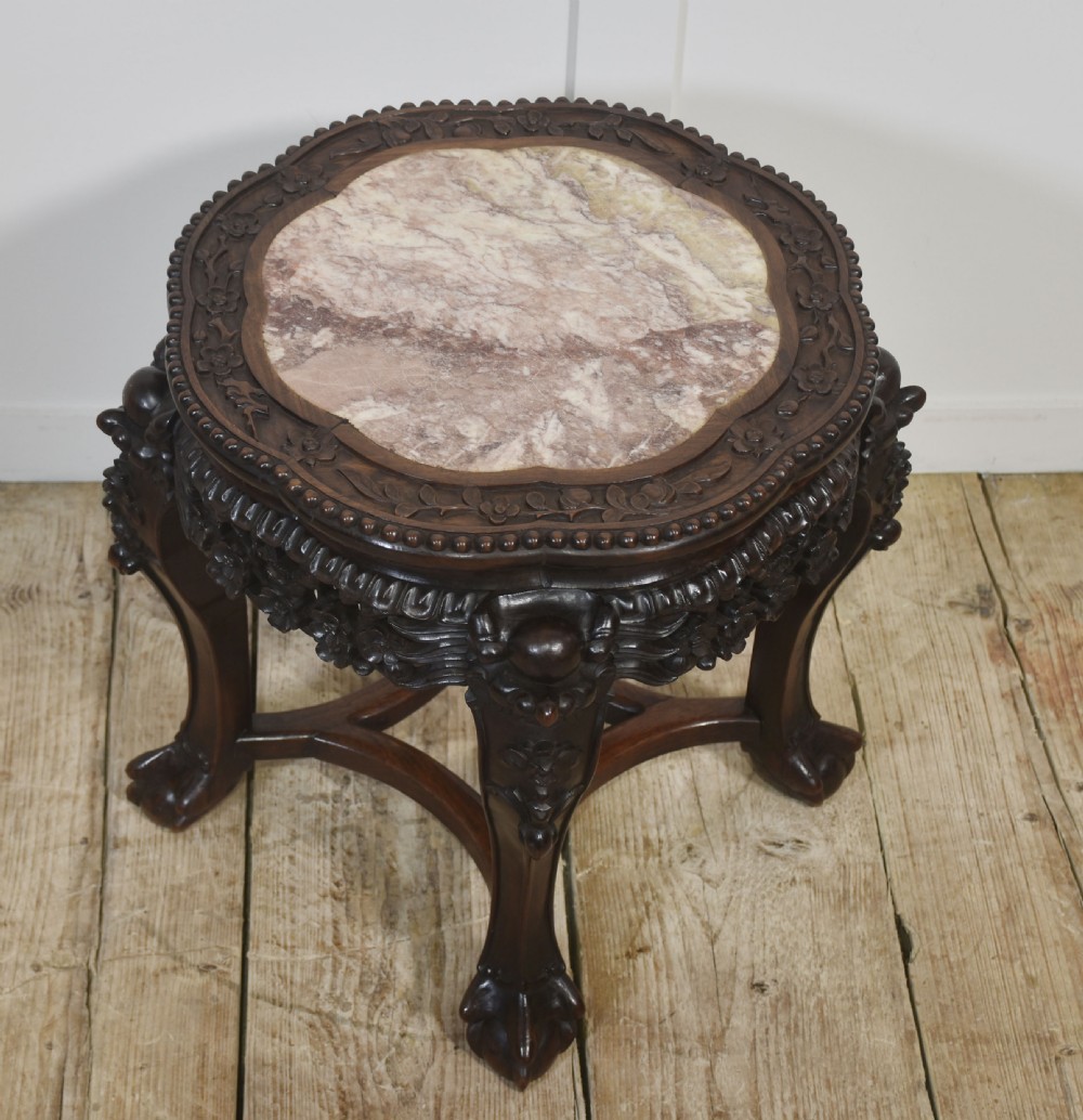 A circular dark rosewood side table featuring an inset pinkish marble top, openwork carved floral apron, cabriole legs, and an X-stretcher. View III