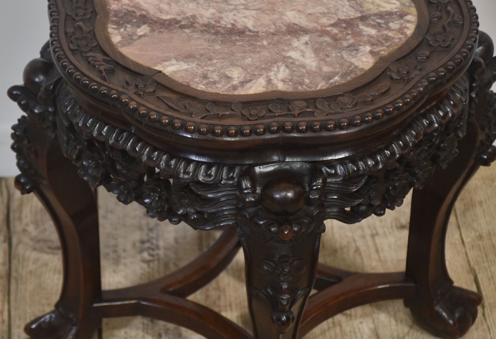 A circular dark rosewood side table featuring an inset pinkish marble top, openwork carved floral apron, cabriole legs, and an X-stretcher. View V