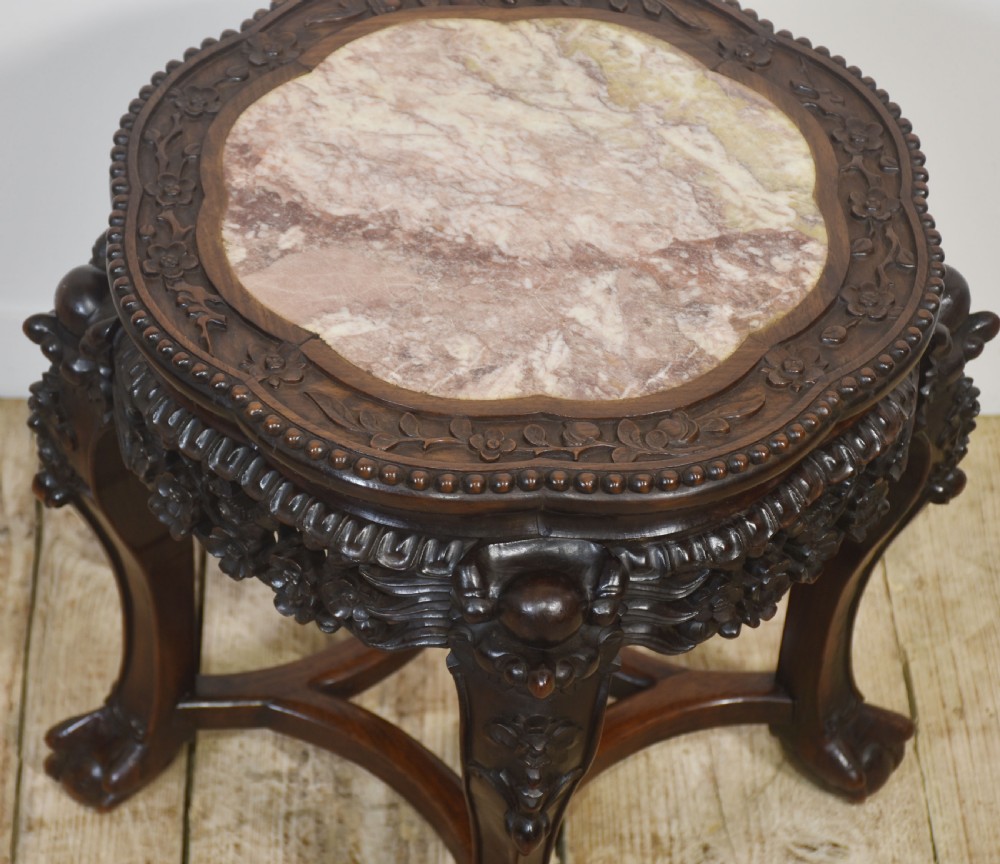 A circular dark rosewood side table featuring an inset pinkish marble top, openwork carved floral apron, cabriole legs, and an X-stretcher. View VII