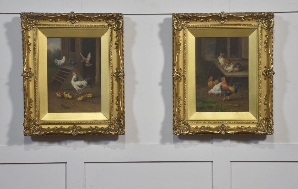 A pair of oil paintings on board depicting farmyard chickens, pigeons, and rabbits inside ornate gold gilt frames.