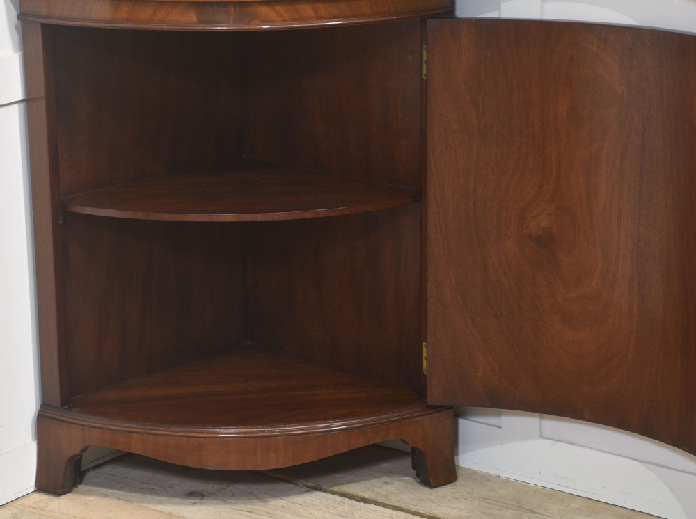A floor-standing bowfront mahogany corner cabinet featuring a curved upper glass door with gothic astragal glazing and a flame mahogany lower cupboard door. View IX