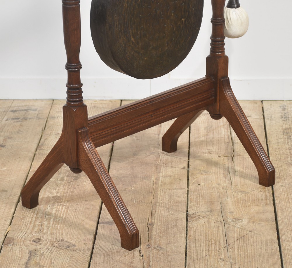 An antique dark oak floor-standing dinner gong featuring turned upright supports, top finials, a suspended circular metal disc, and an attached padded striker. View VI