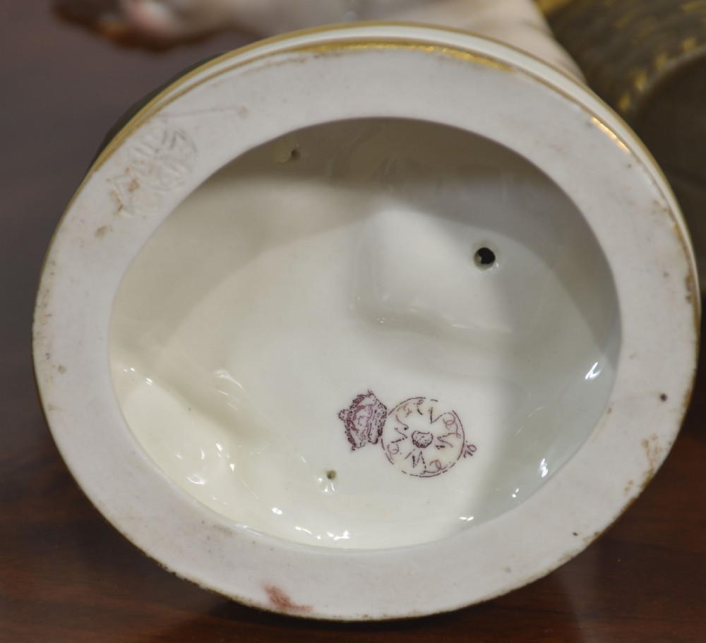 A glazed porcelain figure depicting a cherub carrying a woven basket on its back with gilded details on a circular base. View VII